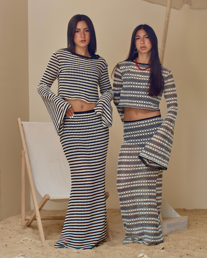 Two women wearing matching black and white patterned outfits standing in a minimalistic setting.
